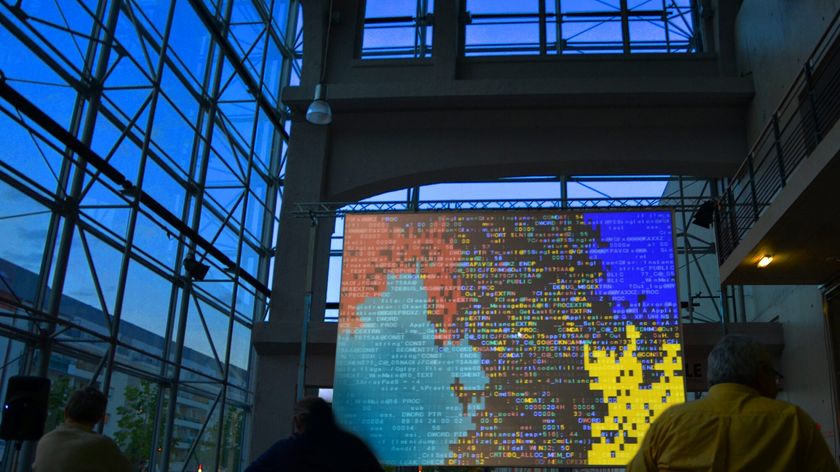 Photograph of a screen displaying a video projection inside the atrium of a glass building.