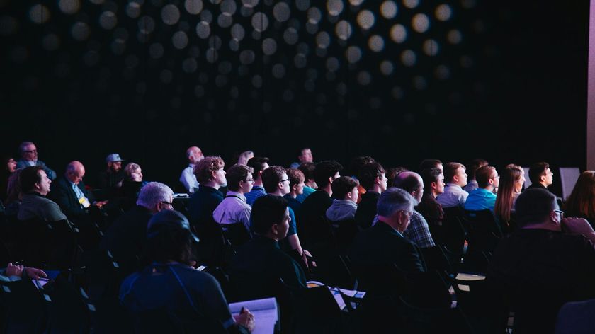 Audience seated in a hall listening to a presentation.