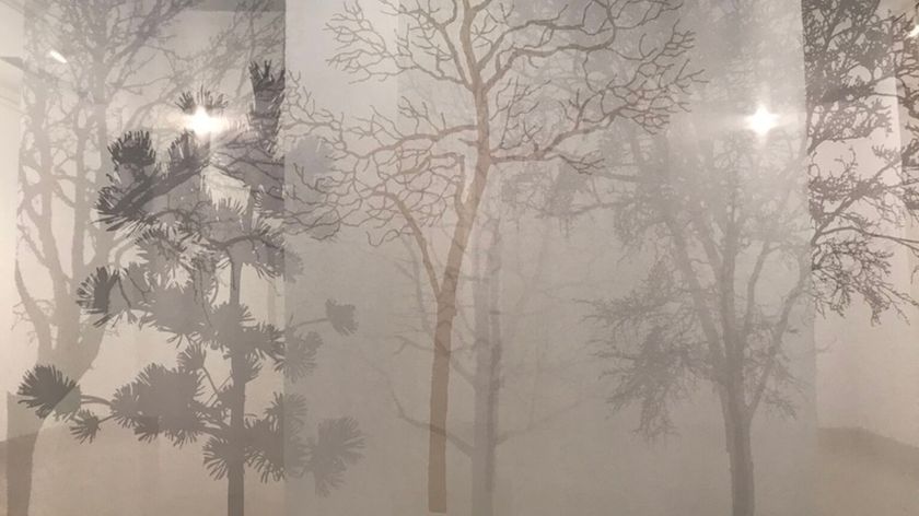Photograph of an installation detail featuring tree silhouettes printed on translucent film, with overlapping flat layers creating the impression of a forest shrouded in fog.