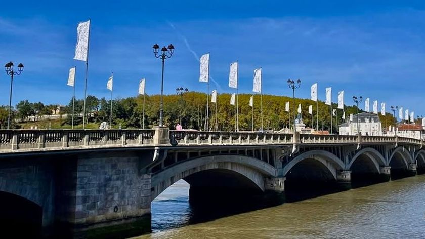 Esprit in Bayonne, a vaulted bridge lined with two rows of white flags featuring graphic designs as part of a public art installation.
