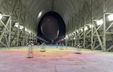 Photograph of a vast interior space containing a large black airship, with an acoustic installation of ten sculptures arranged across the foreground. Photograph of a vast interior space containing a large black airship, with an acoustic installation of ten sculptures arranged across the foreground.